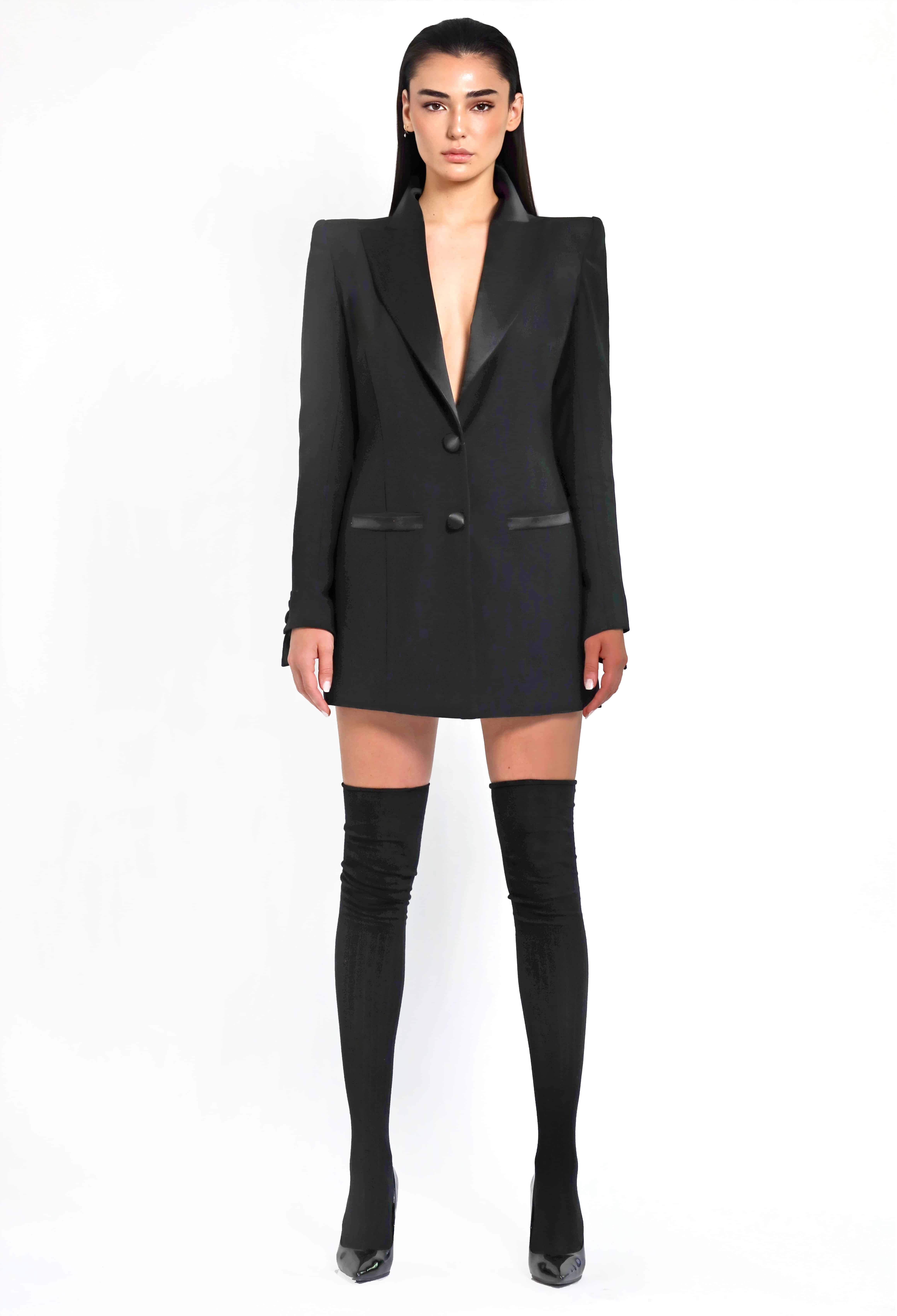 Modelo luciendo el blazer negro. Completa el look con botas altas negras ajustadas, creando un conjunto elegante y moderno.