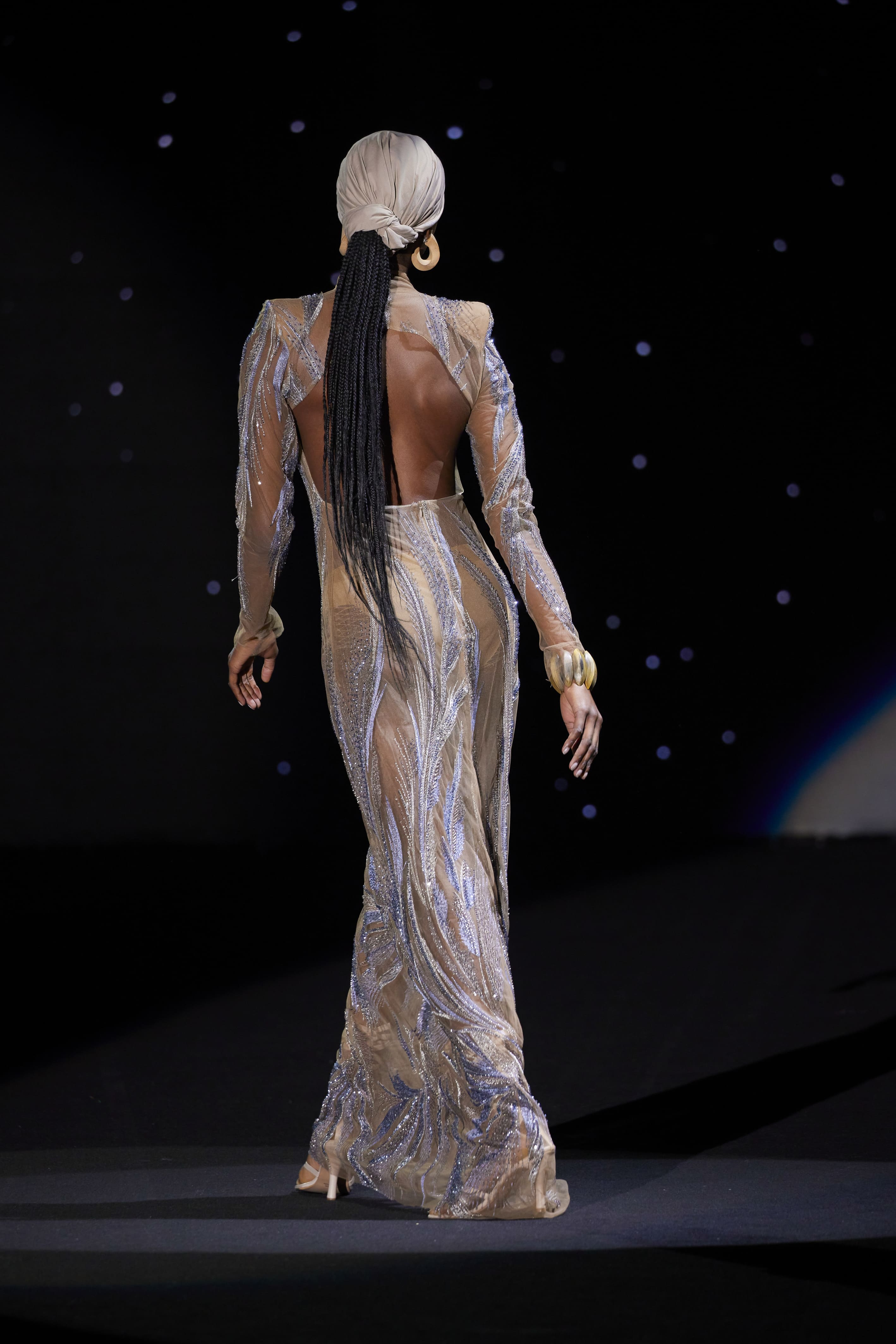 Rear view of a long Malne dress in a nude gold tone with wavy glitter embroidery and a completely open back.