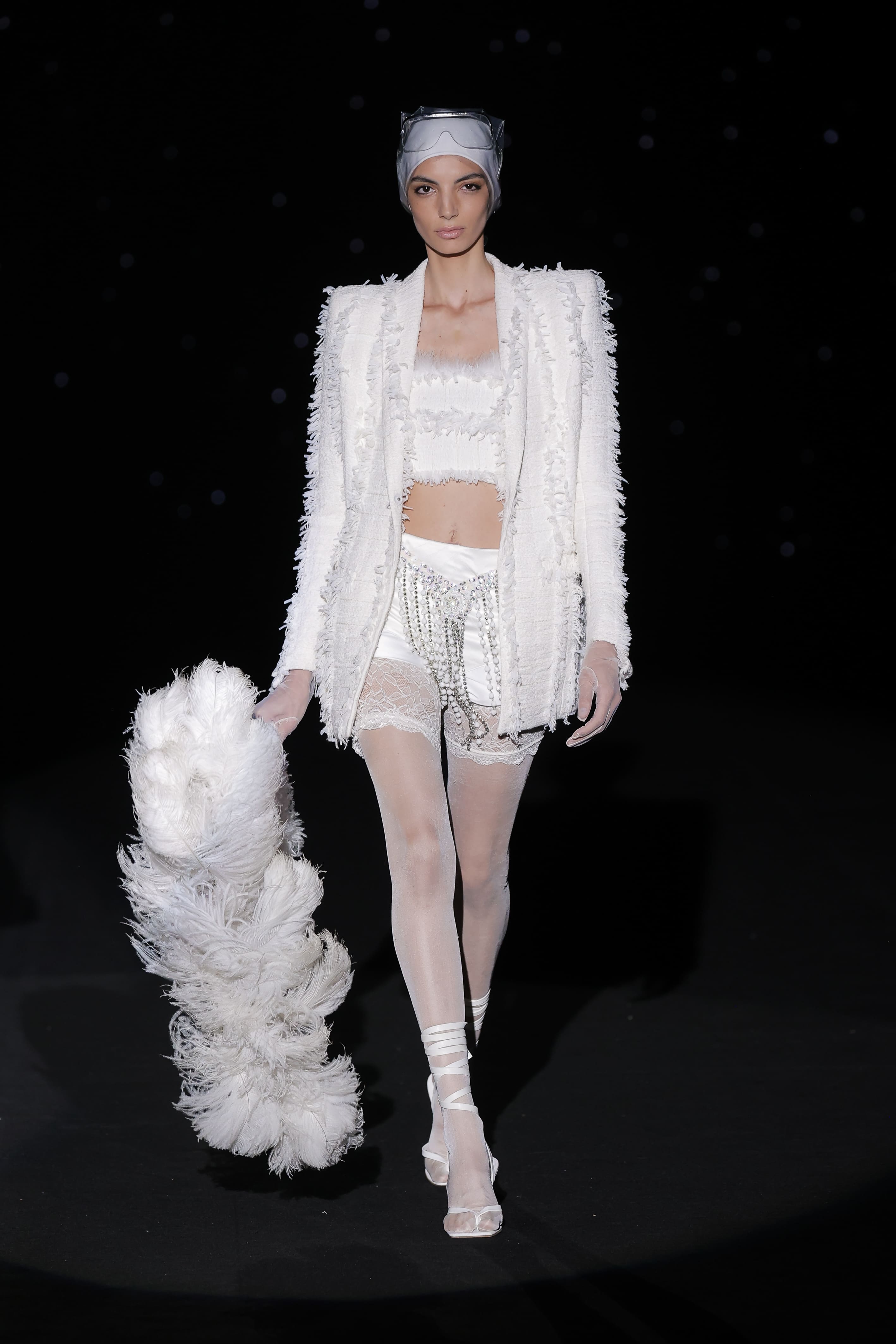 This look exudes an aura of dreamlike sophistication, where white becomes a language of avant-garde and desire. The outfit combines a structured jacket with an almost sculptural fringed texture and a matching cropped top that gives a natural glimpse of skin.
