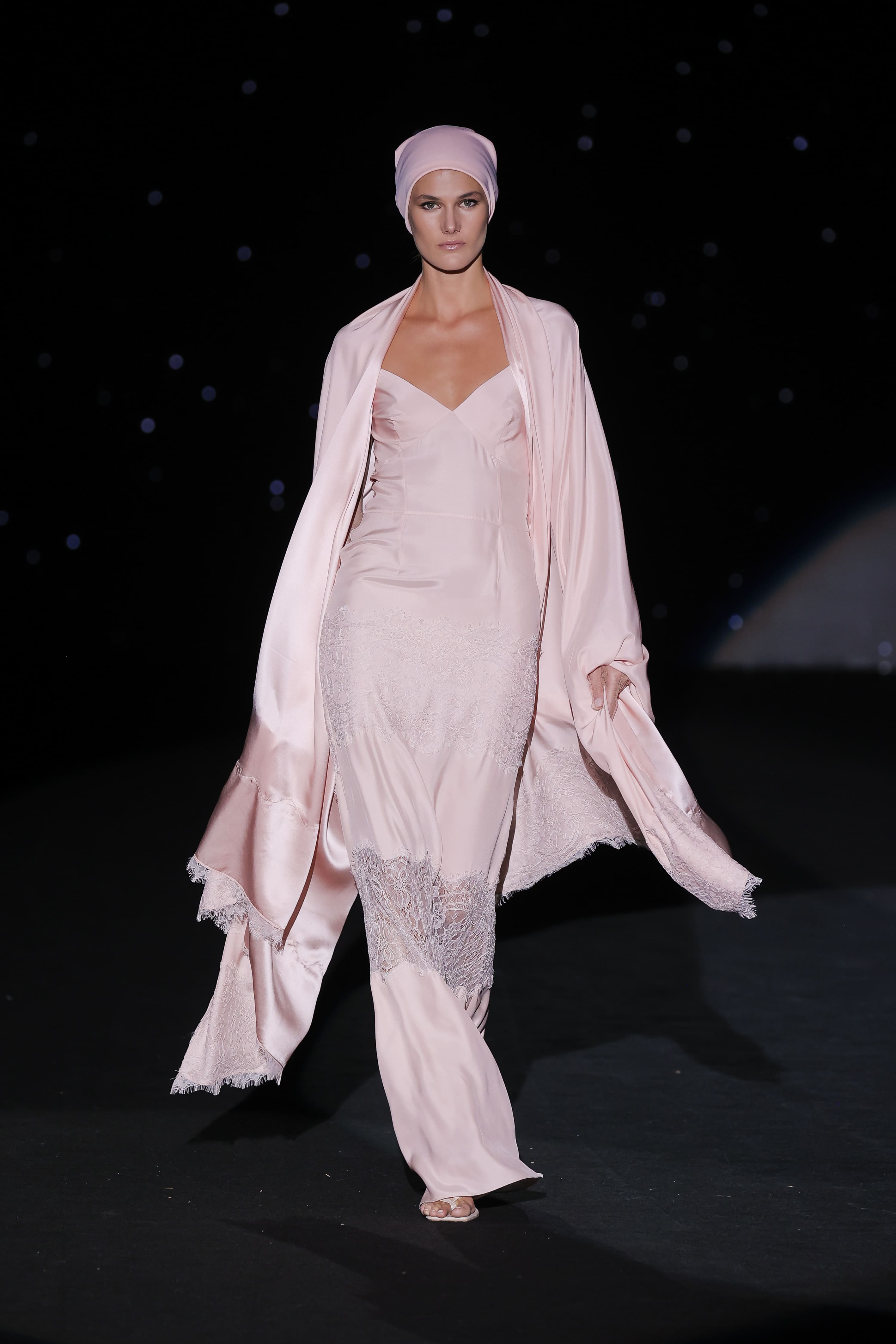Long dress in powder pink satin is the definition of ethereal elegance. Its flowing cut gently hugs the silhouette, while sheer lace details at the bottom add a touch of delicacy and sensuality, playing with light and movement.