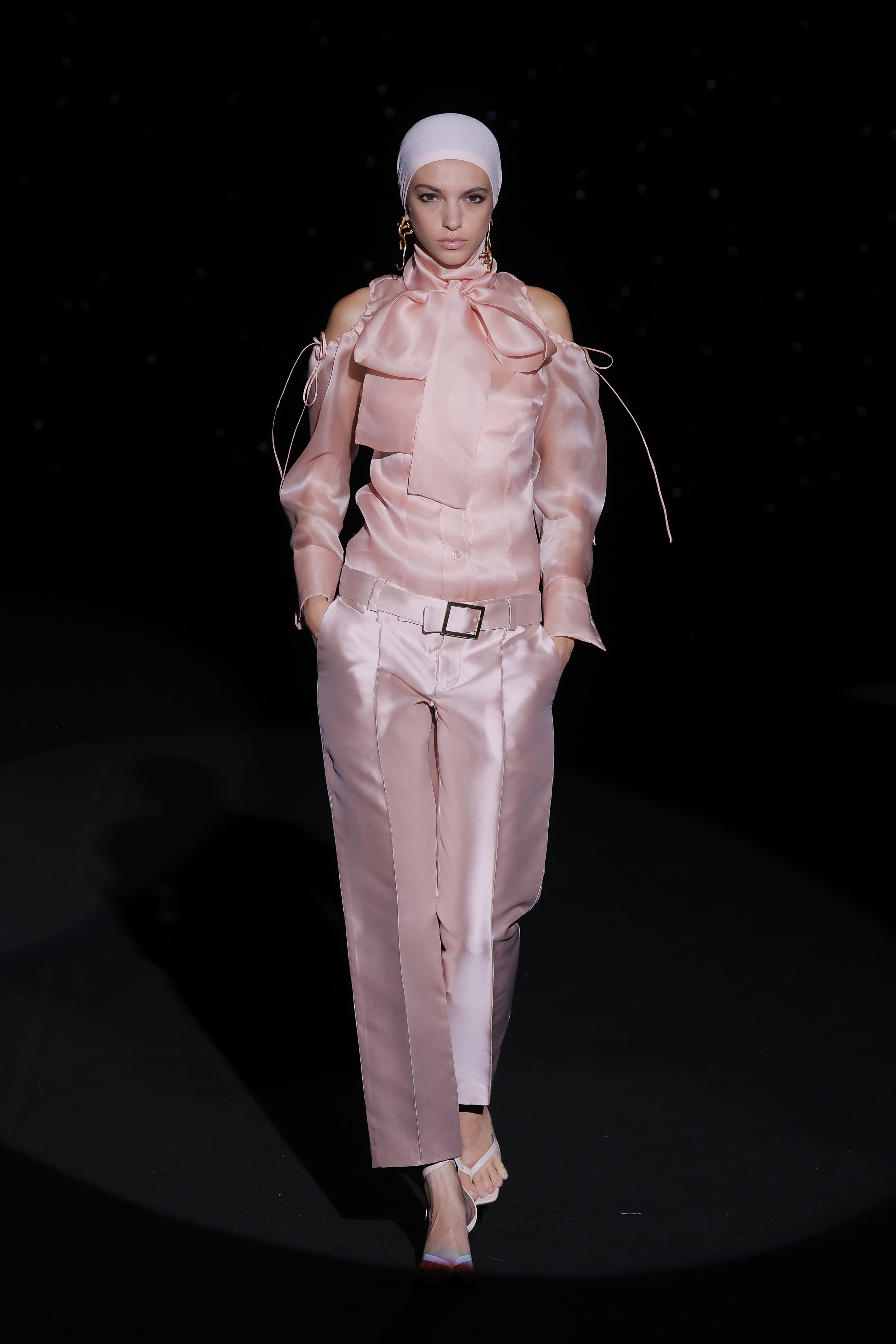 This powder pink satin blouse and trousers set exudes sophistication and femininity with a modern twist. The off-the-shoulder blouse with its puffed sleeves adds a delicate, romantic feel, while the large bow at the neck adds a striking, elegant detail, evoking a classic style with a contemporary twist.