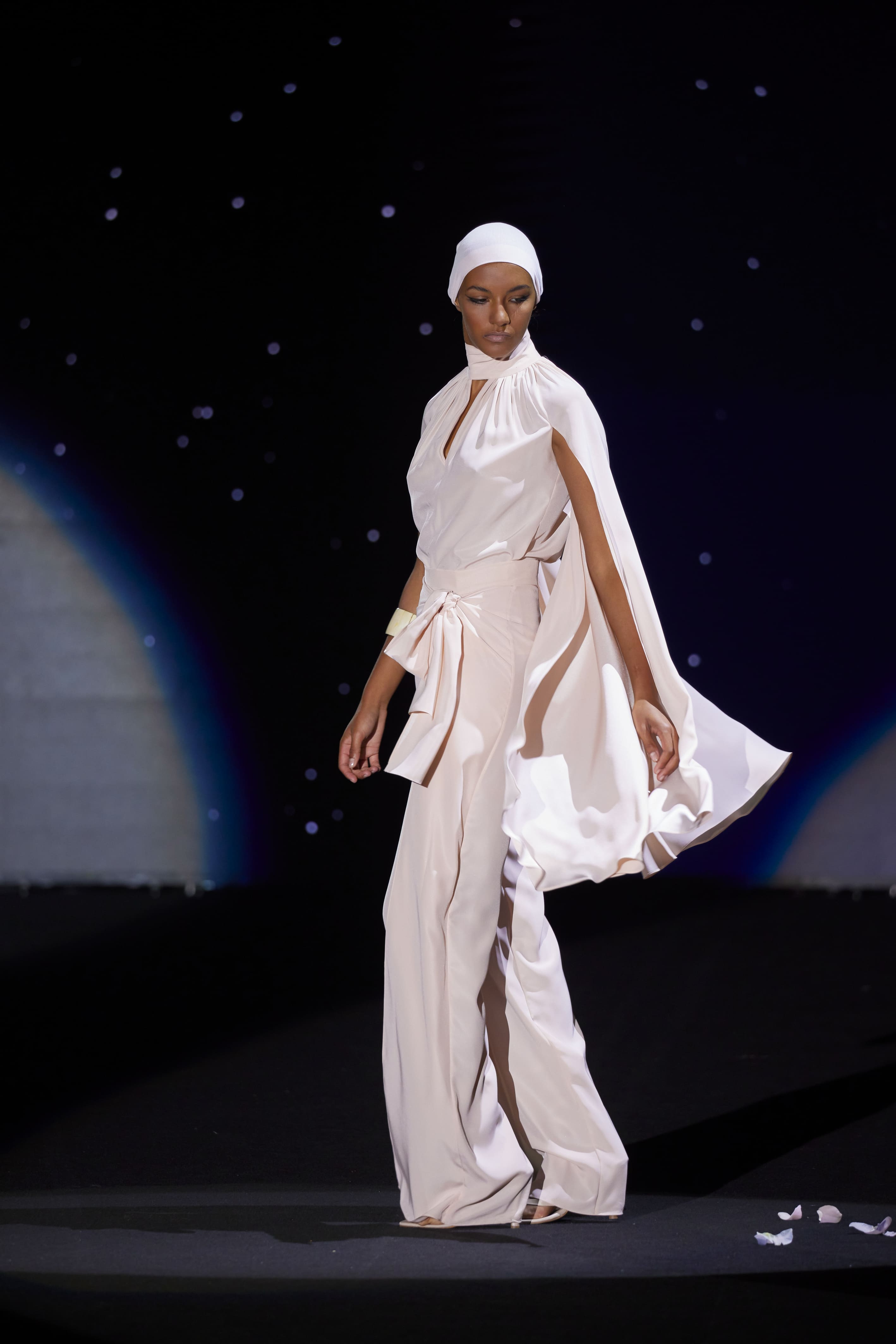 This pastel-pink couture ensemble is a flowing, contemporary sophistication. The blouse is crafted in a lightweight satin, with a pleated high-neck design and a wide cape that falls from the shoulders, bringing movement and elegance to the walk.