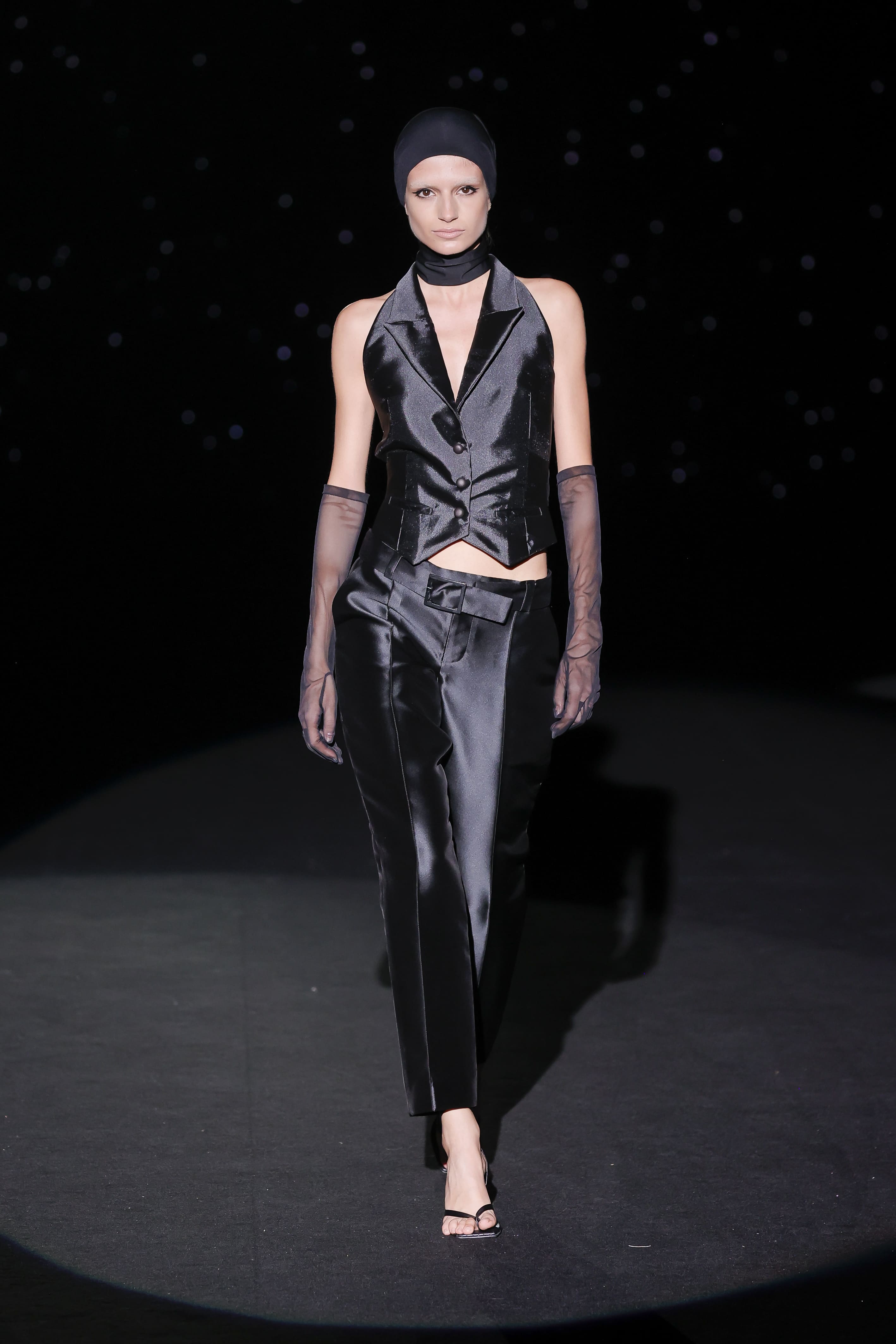 sublime to the power of tailoring and restrained seduction. This masculine-inspired ensemble reinterprets the dinner jacket with a nocturnal, satin vision, where the waistcoat with its sharp lapels and precise buttoning clings to the torso like liquid armour.
