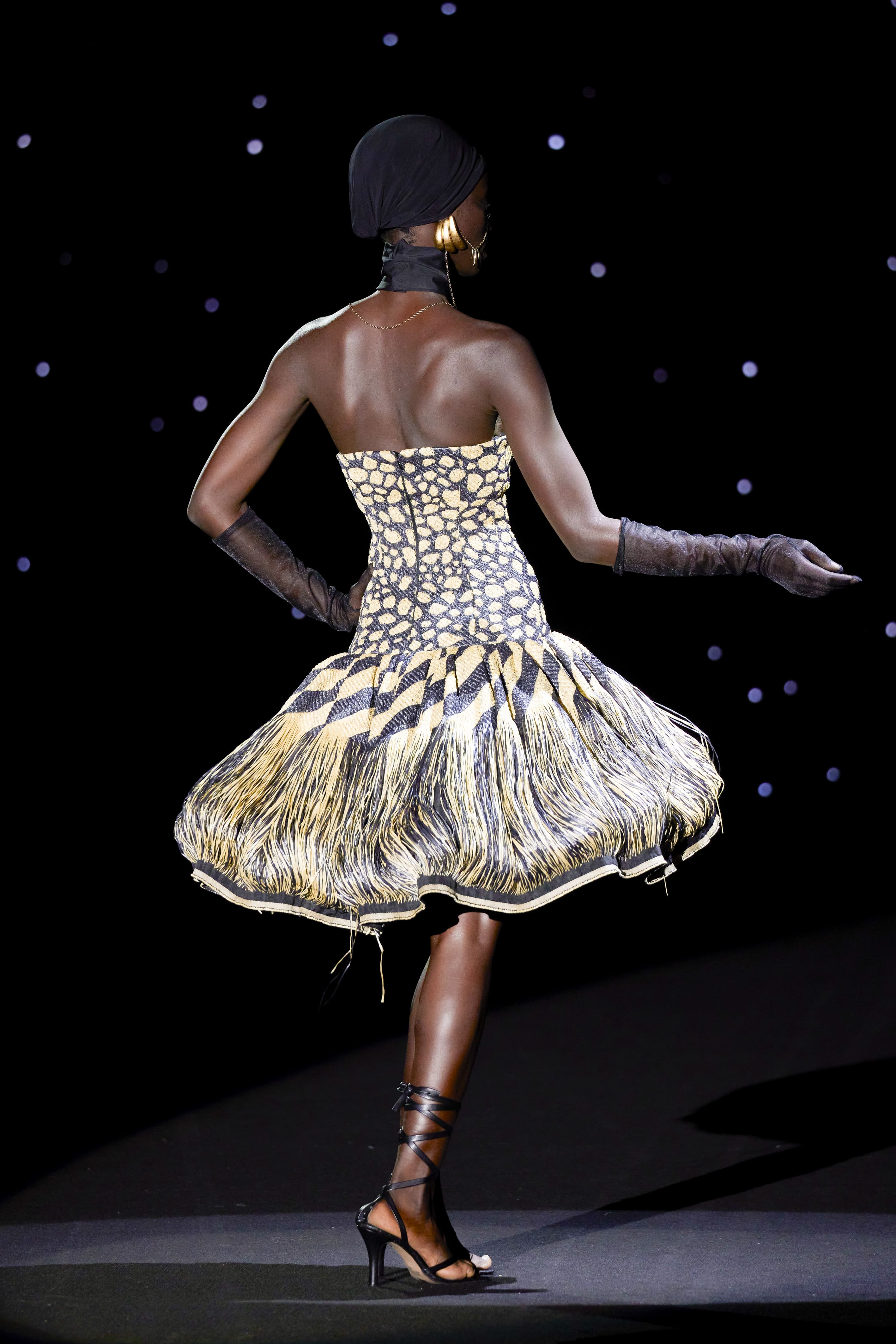 silhouette seen from the back reveals the full sculptural strength of the design. The fitted bodice hugs the torso with an almost architectural precision, emphasising the body's natural musculature and enhancing the posture with a resounding elegance.