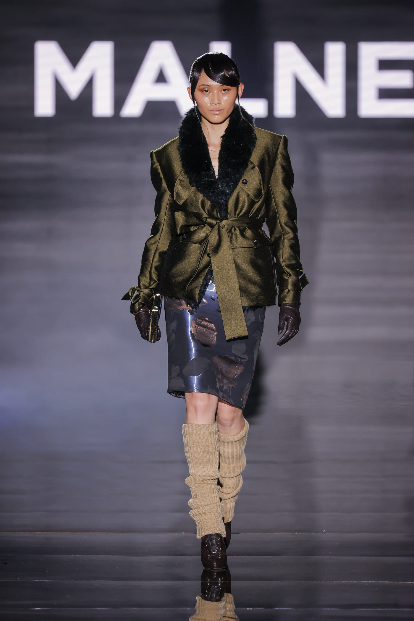catwalk model with black green fur jacket, black flowery skirt and high boots