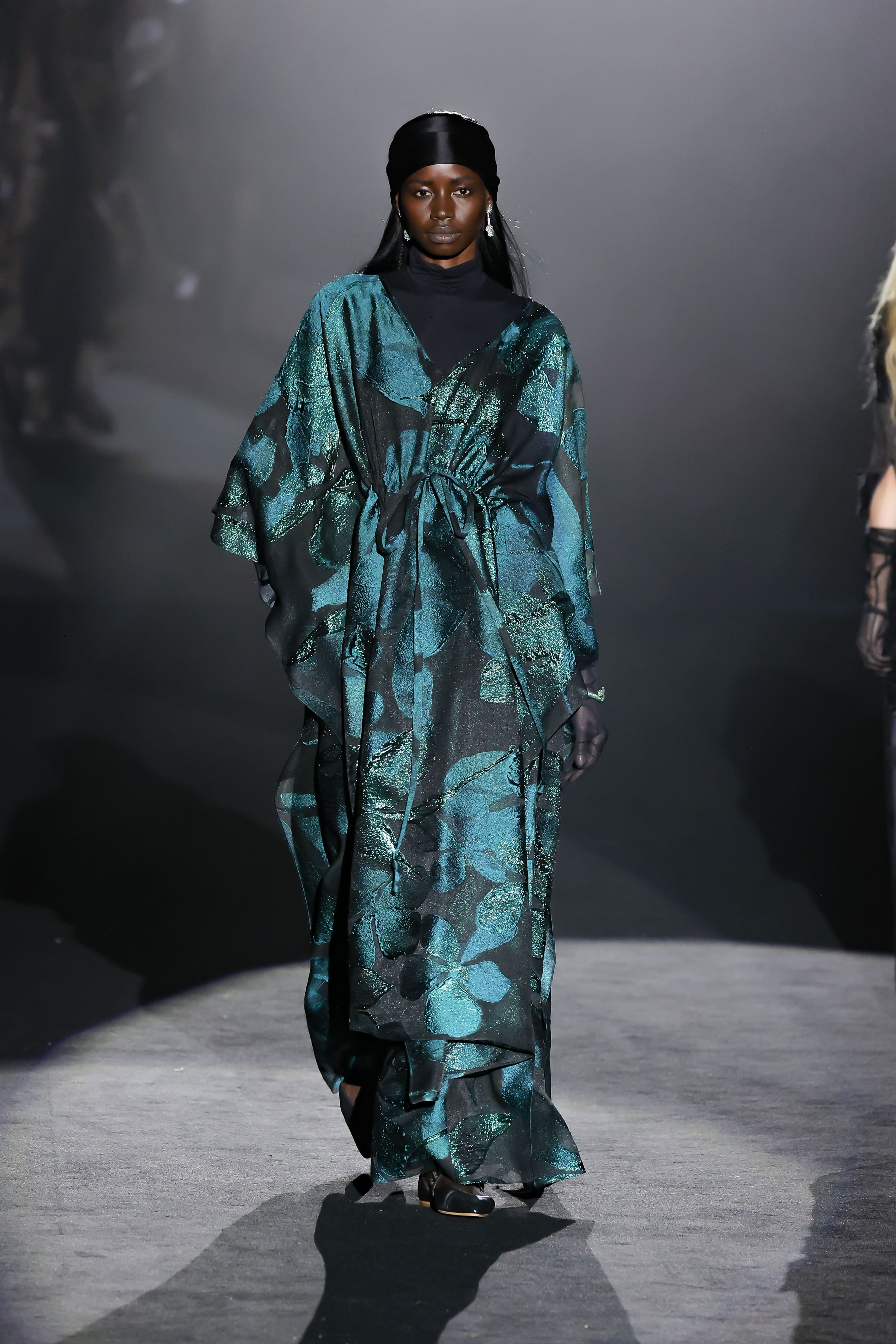The model walked the runway in a long, flowing green dress with a shimmering print.