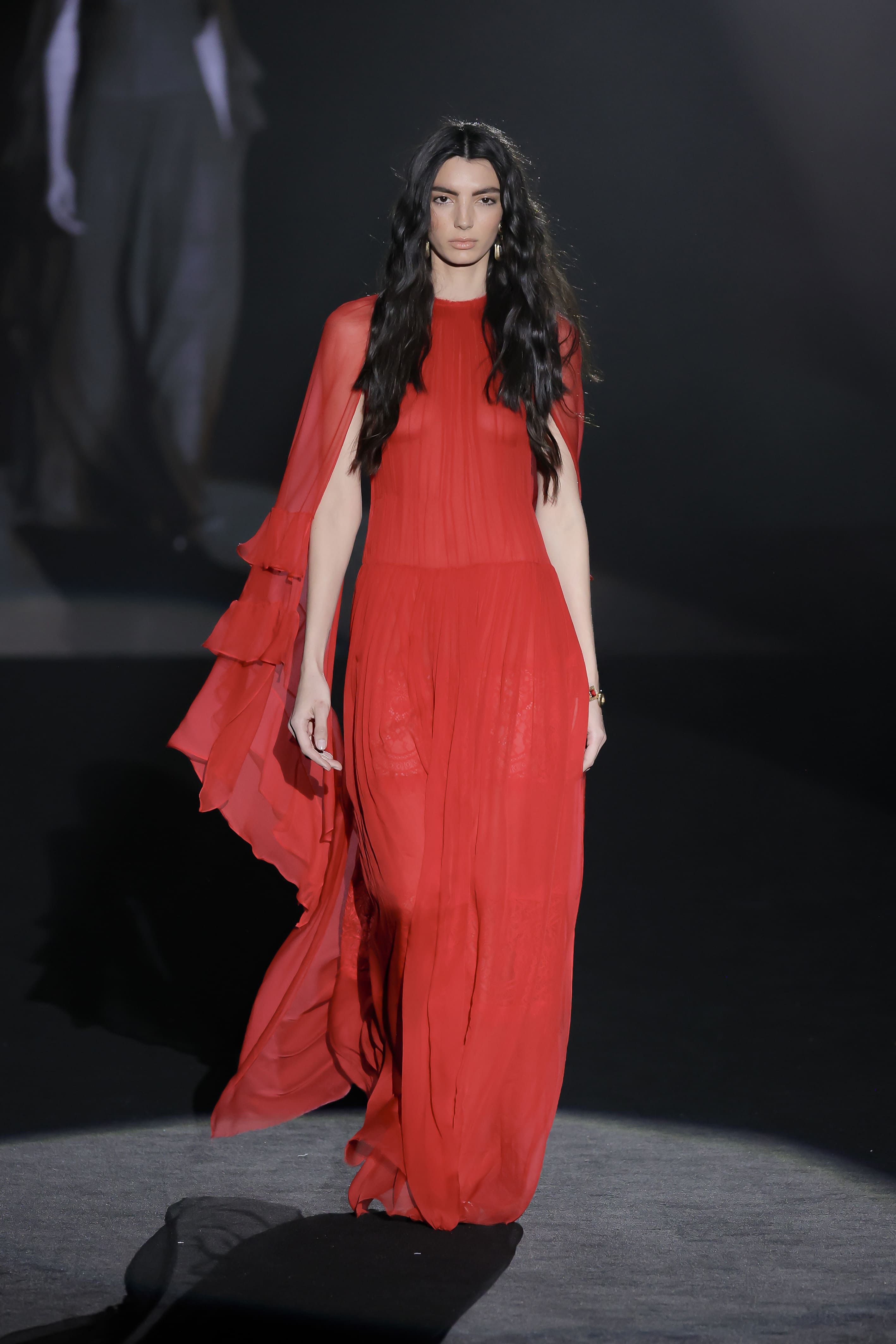 catwalk model The long dress, made of a flowing crimson red fabric, flows naturally and envelops the silhouette in an almost heavenly aura.