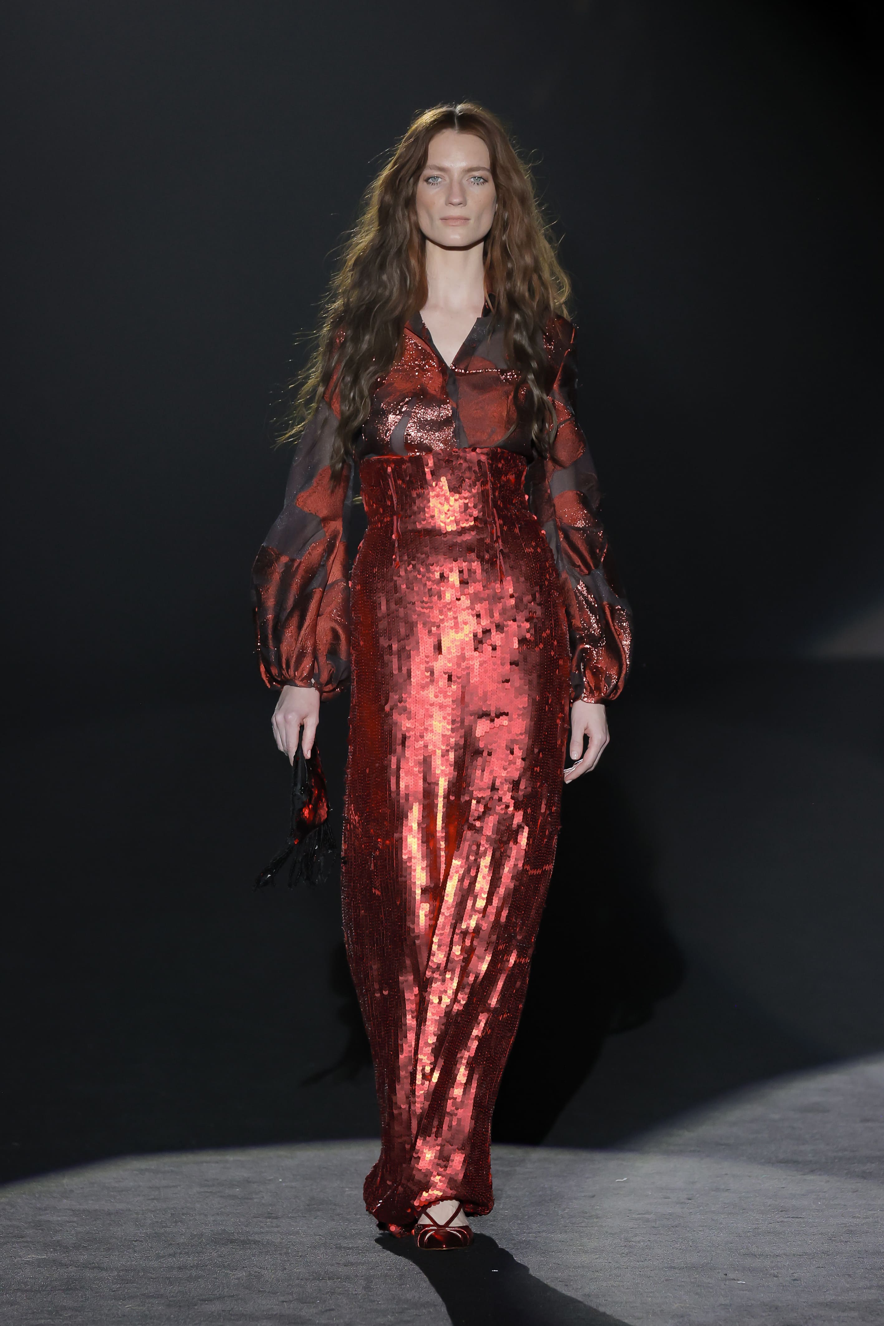 A model walks down the catwalk in a long red sequined dress.
