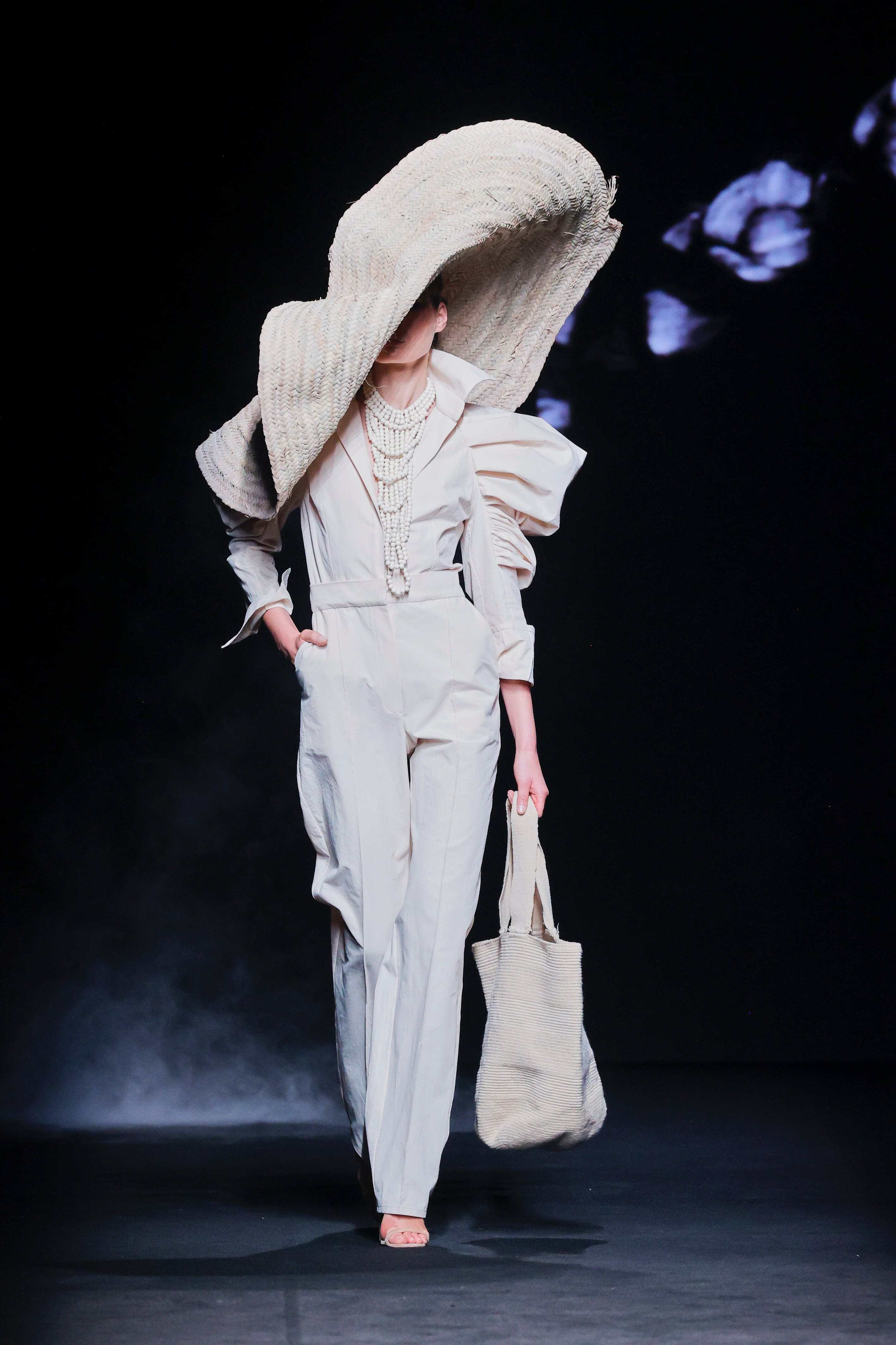 Modelo desfila en la pasarela con un conjunto blanco elegante y un gran sombrero de ala ancha