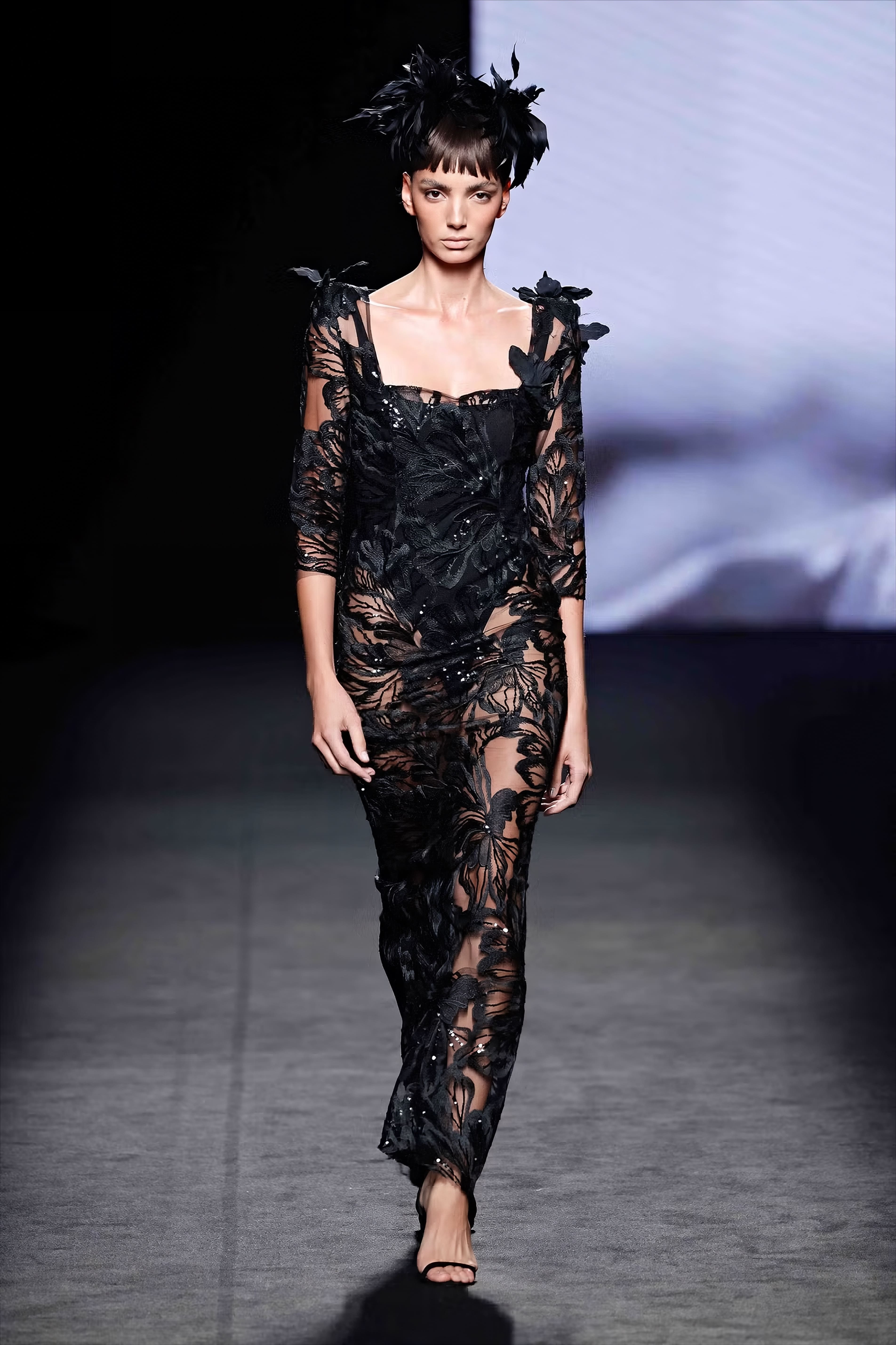Modelo en la pasarela con vestido negro semitransparente de Malne con bordados florales y textura de encaje que deja ver la silueta.