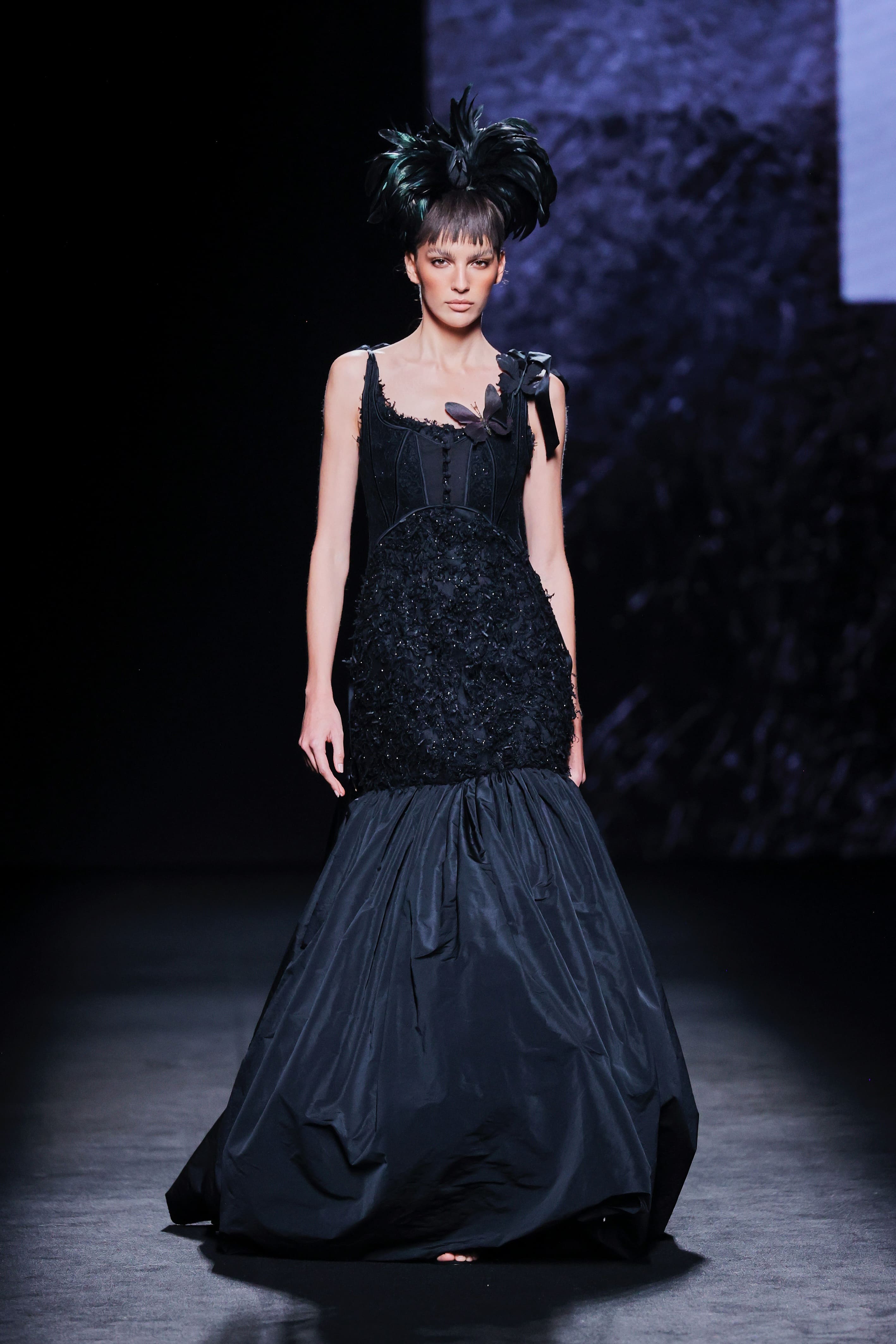 Modelo en la pasarela con vestido negro de Malne de silueta sirena, con cuerpo ajustado de textura rica y falda amplia de gran volumen.