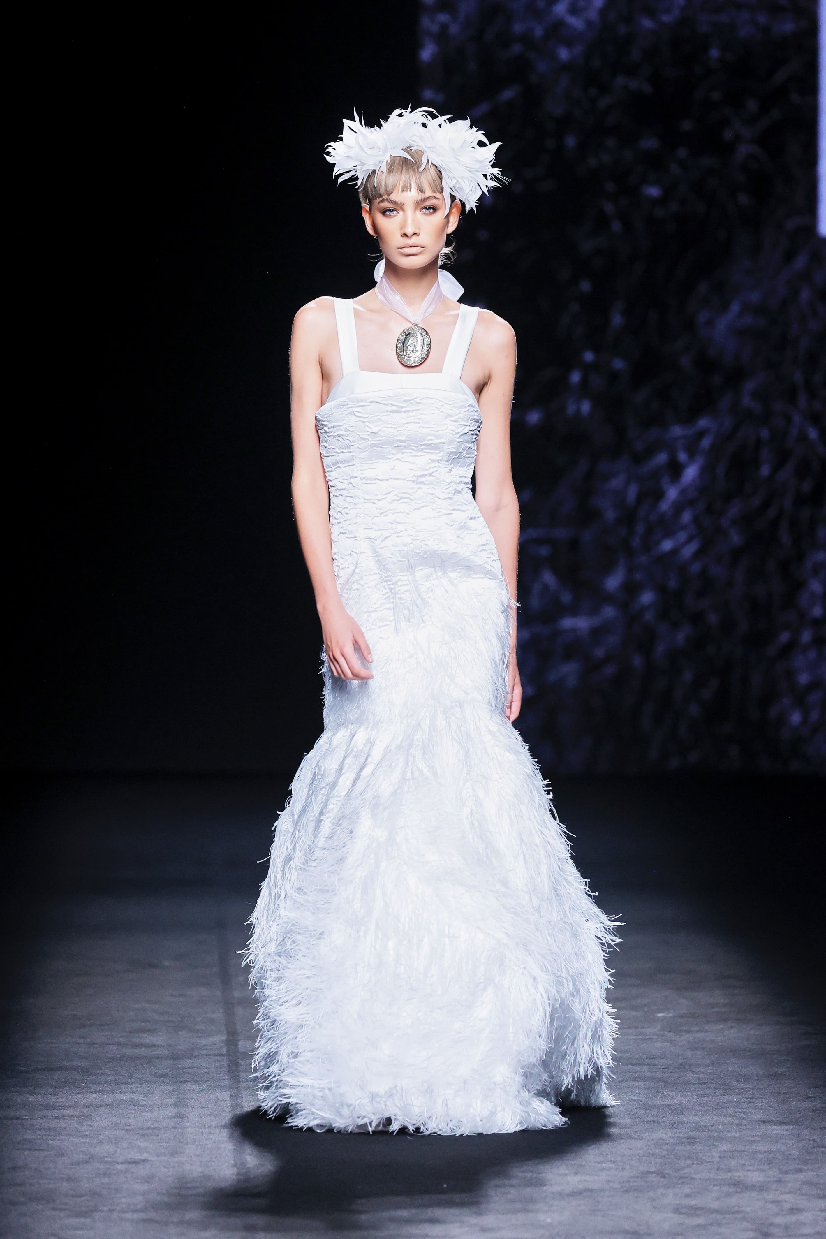 Modelo en la pasarela con vestido largo blanco de Malne de silueta sirena y textura de plumas en la falda.