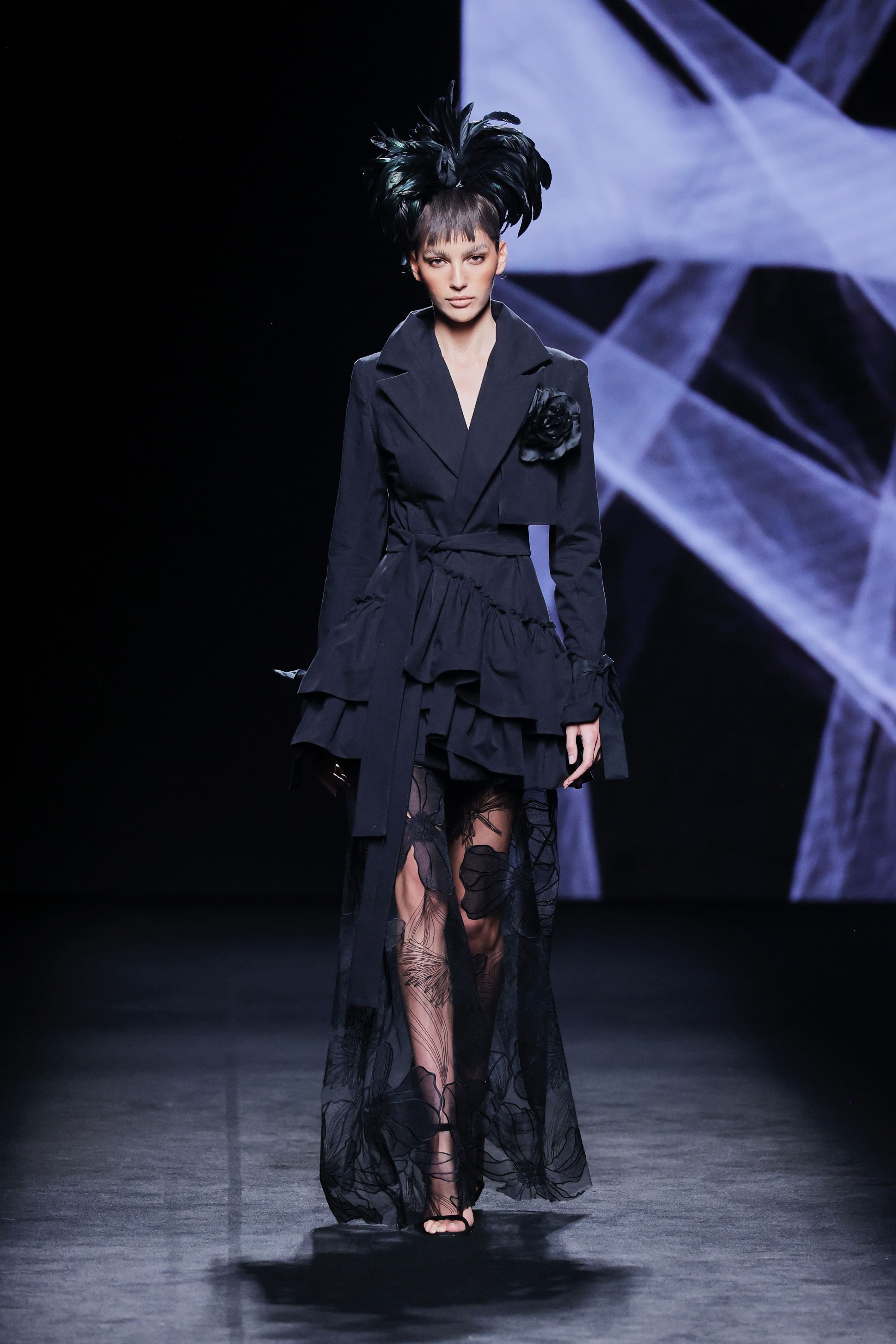 Modelo en la pasarela con conjunto negro de Malne formado por chaqueta entallada con volantes y falda larga de tul semitransparente.