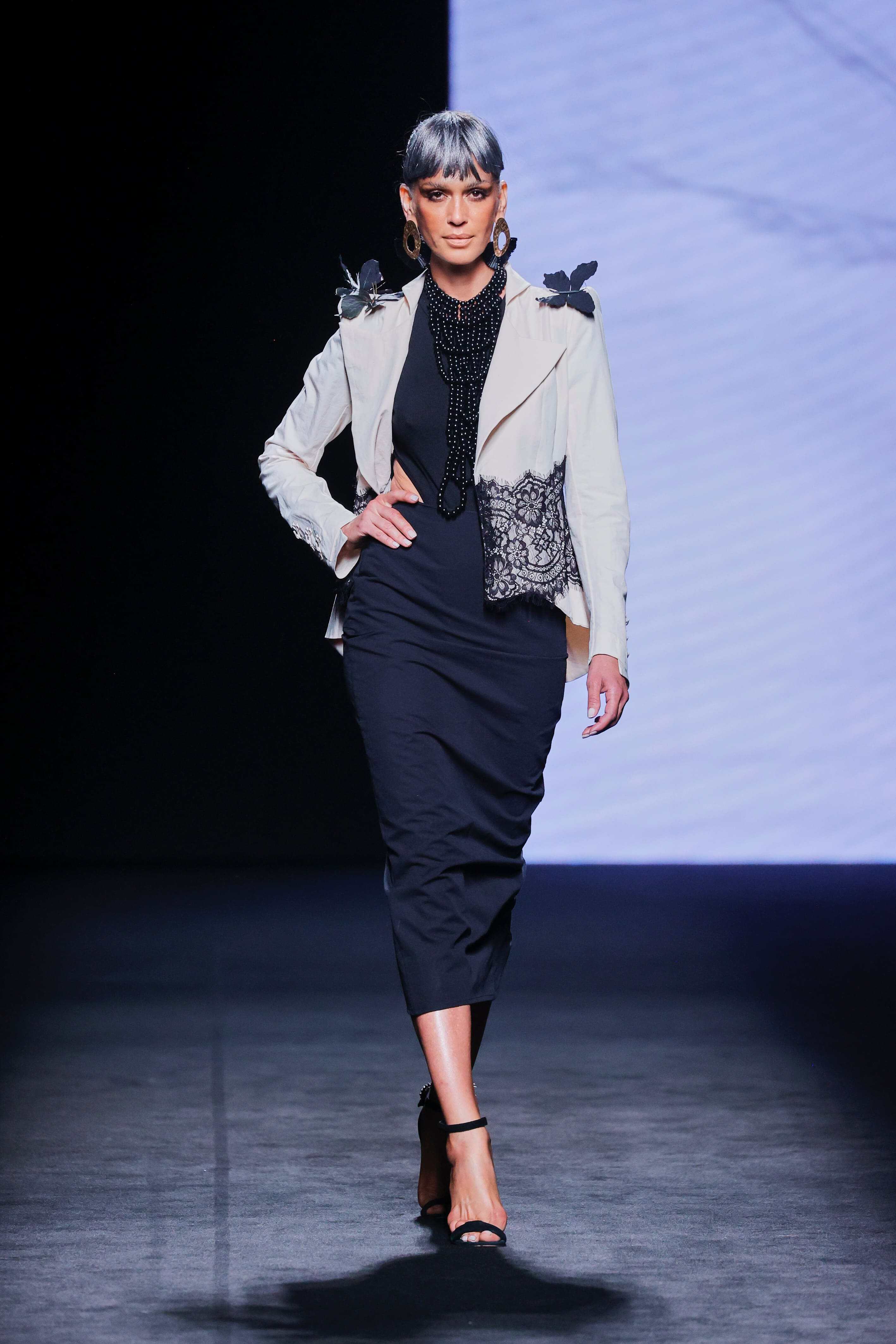 Modelo en la pasarela con vestido negro ajustado de Malne y chaqueta corta color marfil con detalles de encaje negro.
