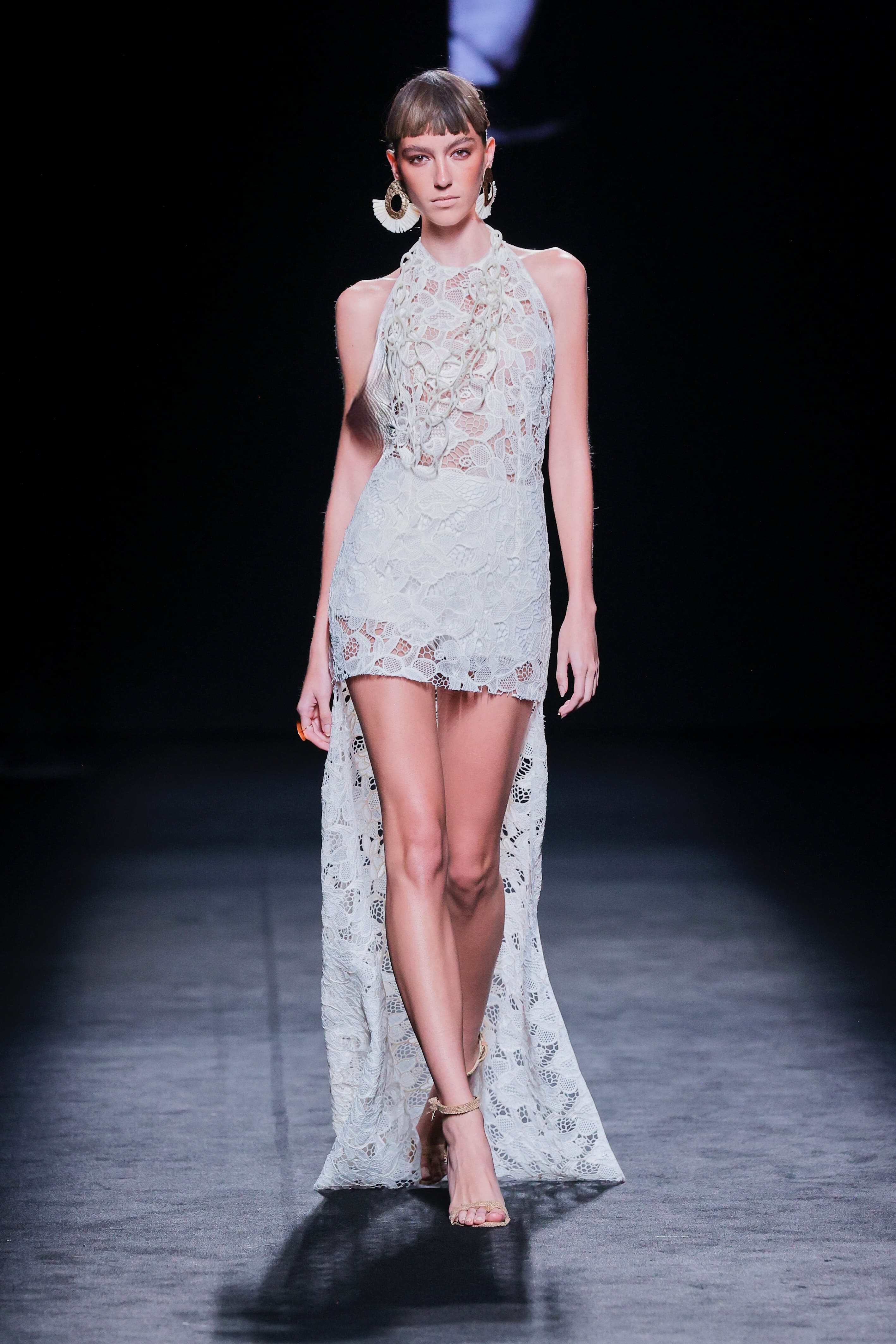 Modelo en la pasarela con vestido blanco de encaje de Malne, corto por delante y largo por detrás.