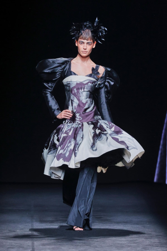 Modelo en pasarela luciendo un vestido estructurado con volumen, en tonos blanco, negro y morado con estampado artístico