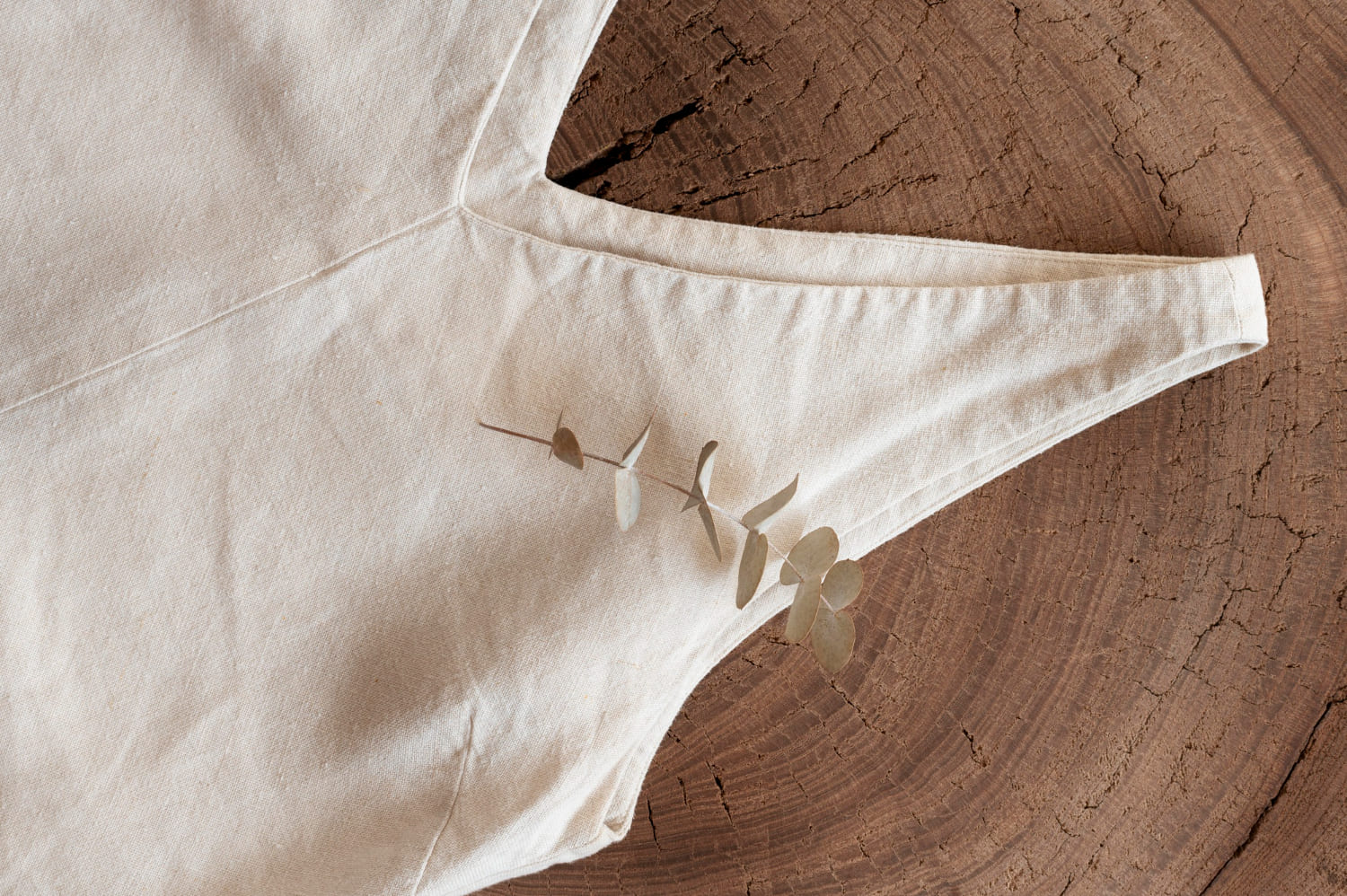 Detalle de prenda en tono marfil con tirante fino y costuras visibles sobre una superficie de madera natural.