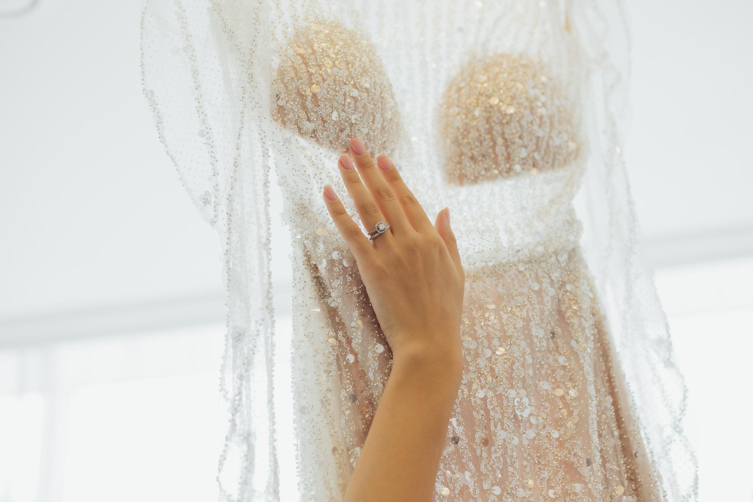 Primer plano de una mano tocando un vestido de novia con pedrería brillante y transparencias