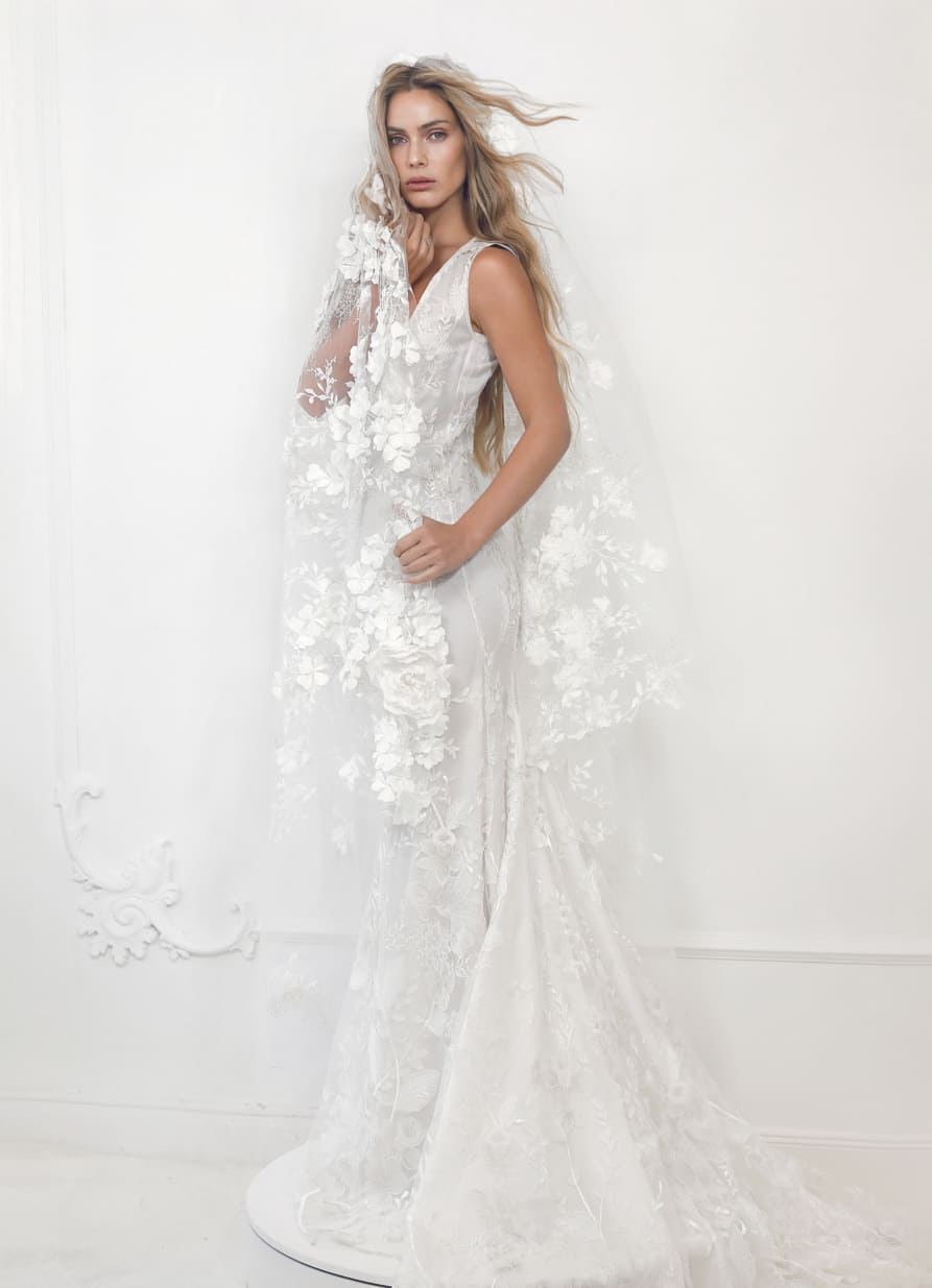 Vestido de novia de Malne en color marfil con silueta entallada, escote en V y largo velo transparente bordado con flores en relieve.