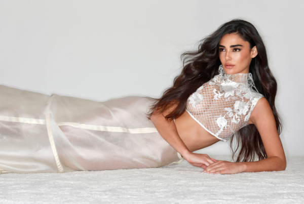 Mujer recostada sobre una superficie clara con vestido largo en tono nude de tejido semitransparente. El diseño presenta bordados florales en relieve en la parte superior y una silueta ajustada que resalta la elegancia y delicadeza del conjunto.