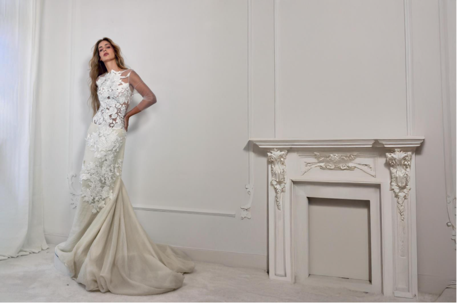 Malne model wearing a white lace dress with a long train in an elegant hall.