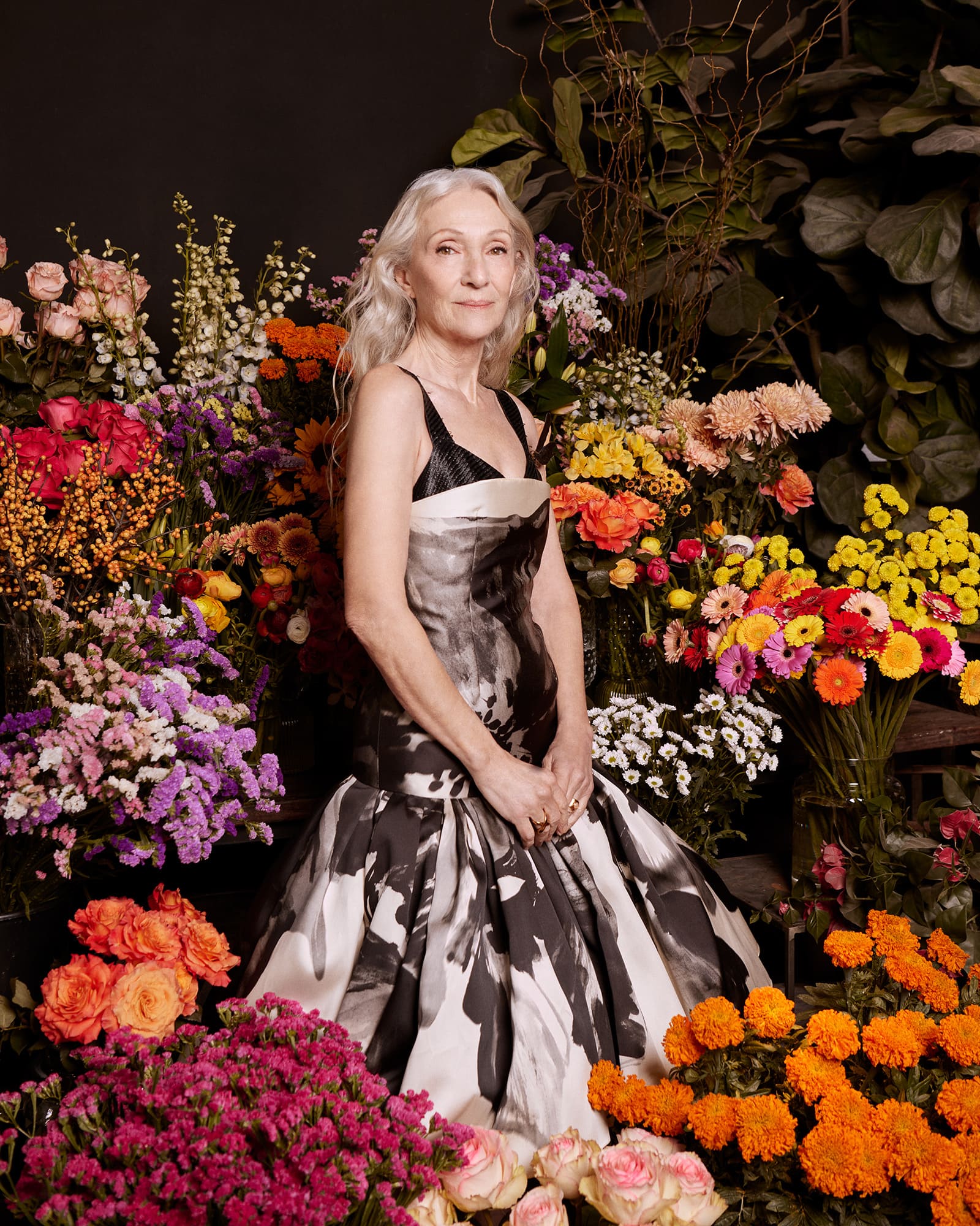 Woman poses in an elegant black and white print dress surrounded by an abundance of colourful floral arrangements.