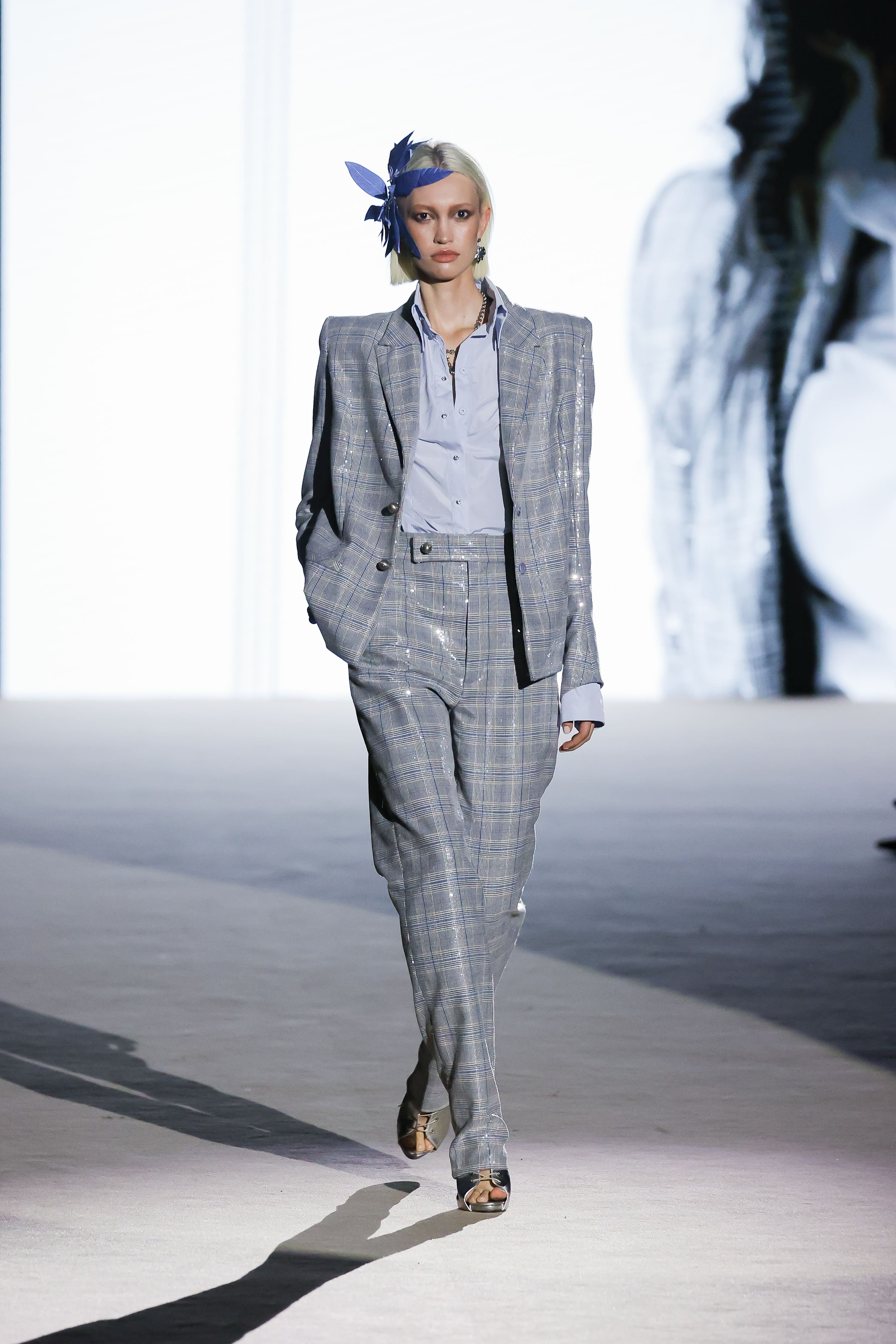 Modelo con traje gris de cuadros y camisa azul de Malne en la Mercedes-Benz Fashion Week Madrid marzo de 2026 con tocado lateral.