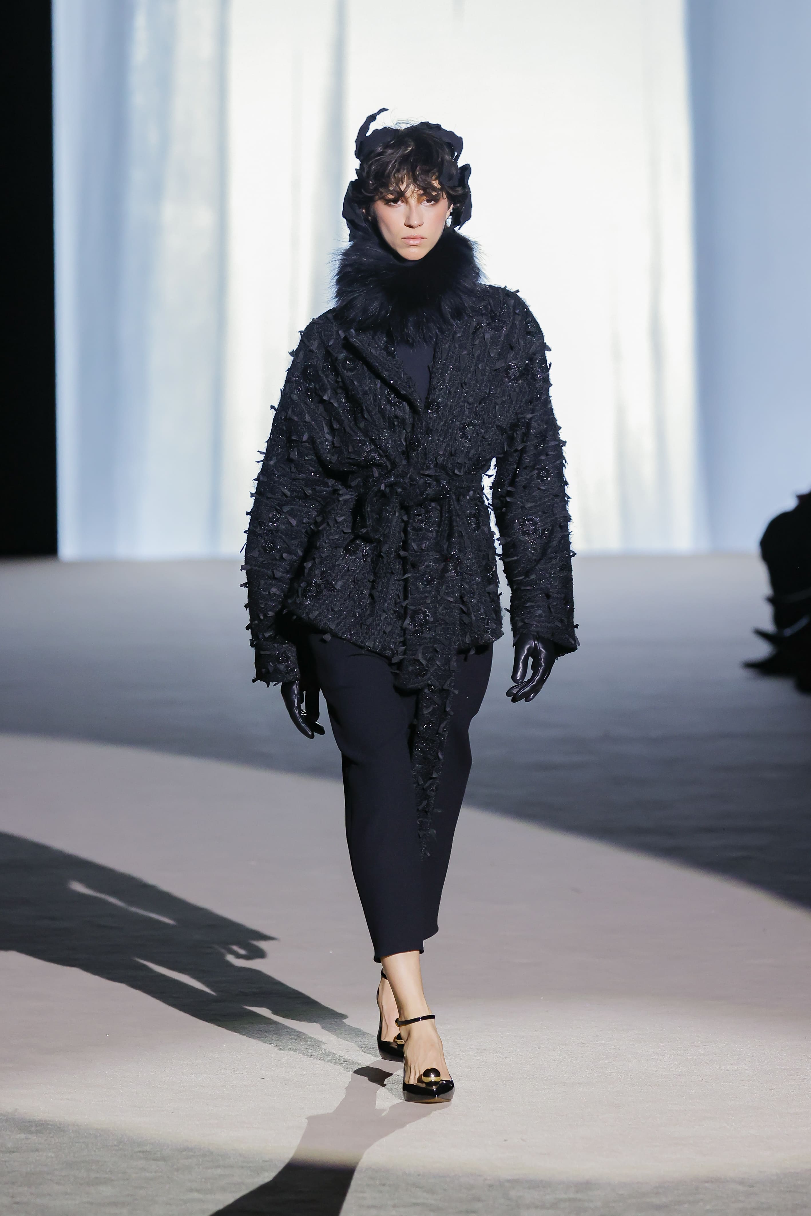 Modelo con abrigo negro texturizado y cuello de pelo de Malne en la Mercedes-Benz Fashion Week Madrid marzo de 2026 con falda recta.