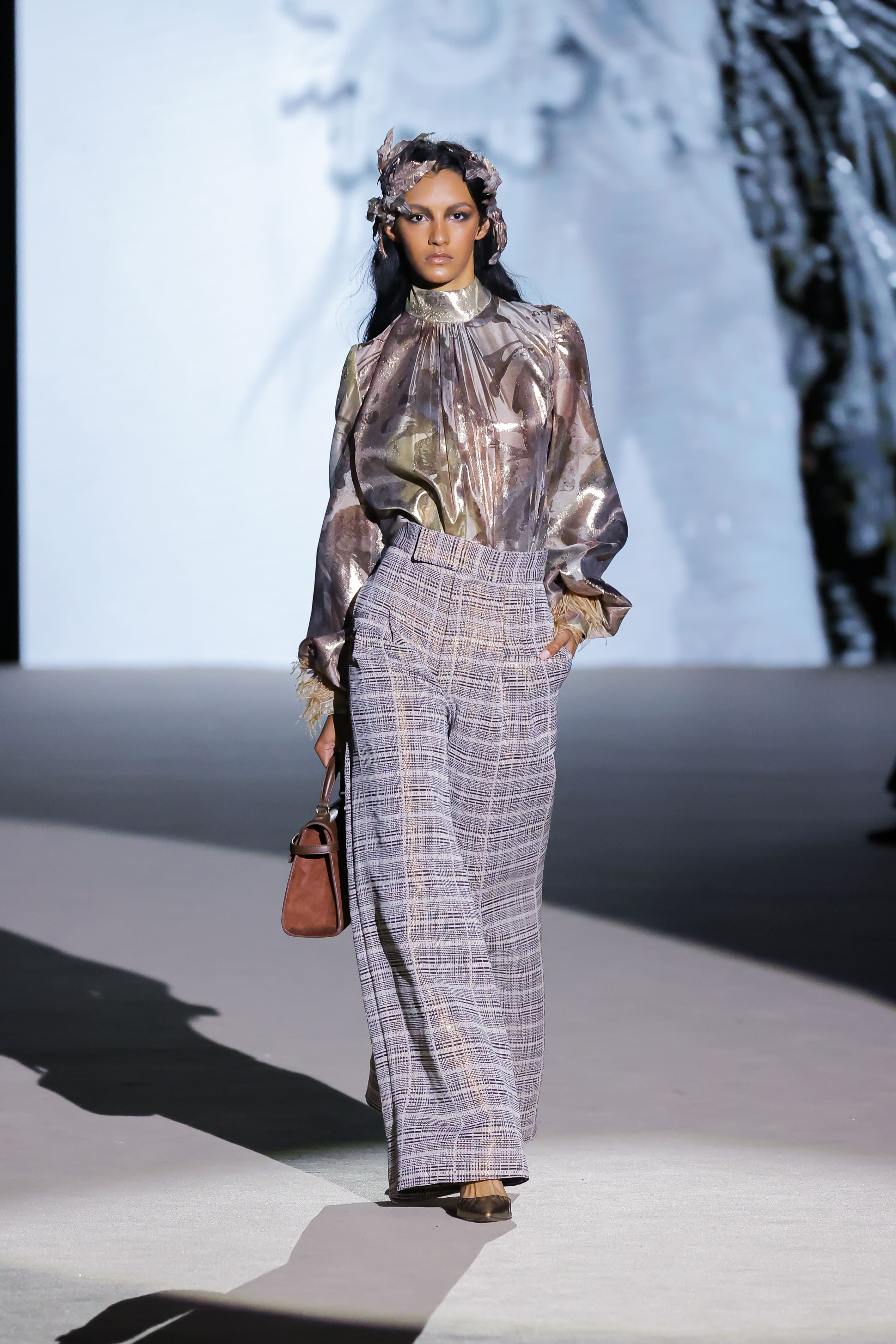 Modelo con blusa satinada estampada y pantalón de cuadros de Malne en la Mercedes-Benz Fashion Week Madrid marzo de 2026 con bolso marrón.