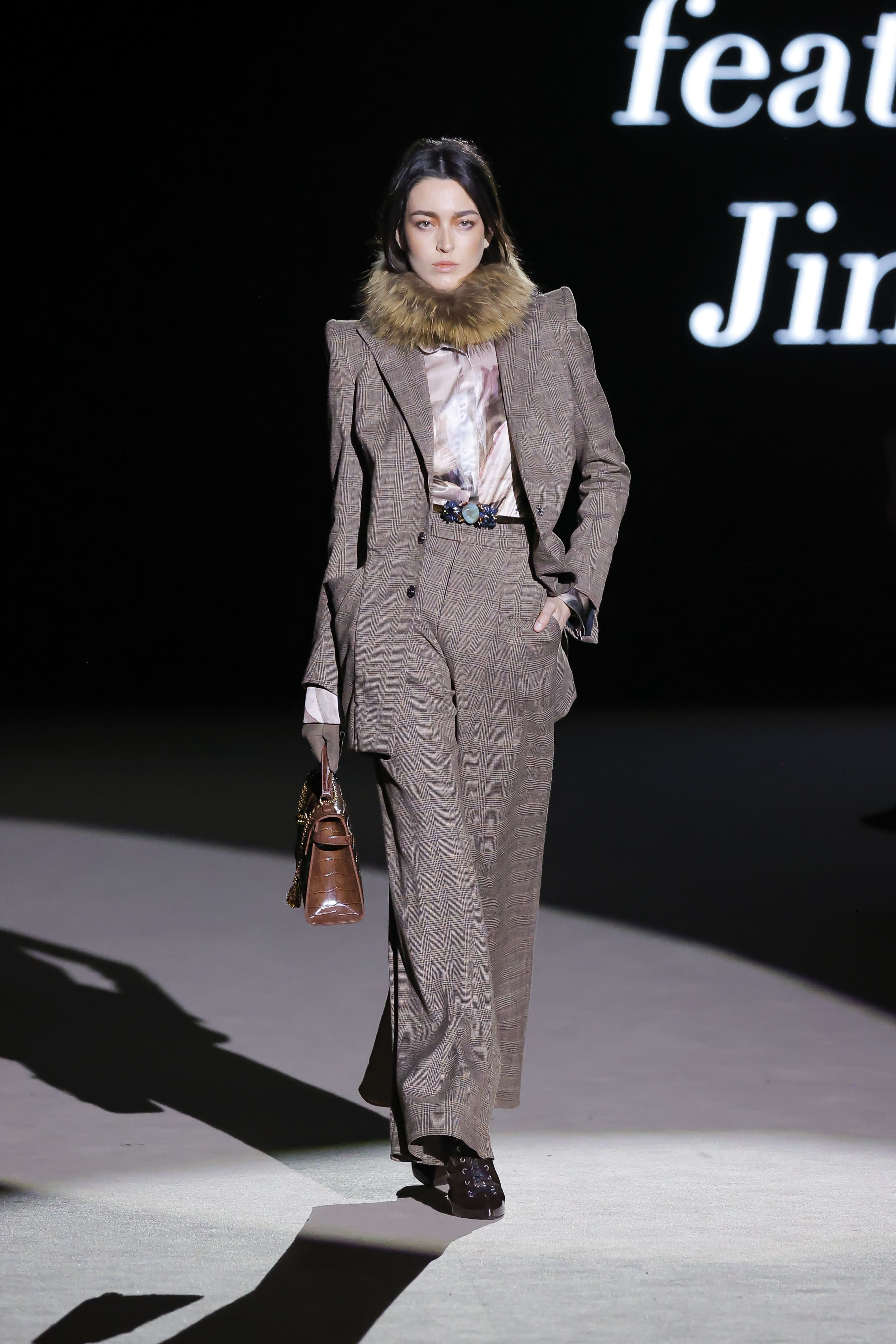 Modelo con traje de cuadros marrón y cuello de pelo de Malne en la Mercedes-Benz Fashion Week Madrid marzo de 2026 llevando bolso estructurado.