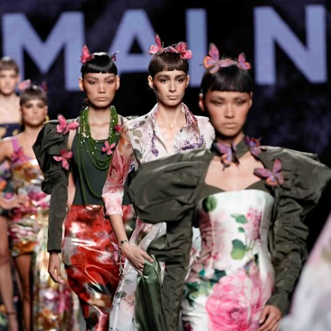 Modelos de Malne desfilan con looks florales y mariposas rosas en el cabello sobre una pasarela oscura.